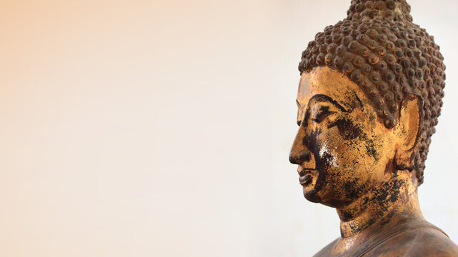 The head of an ancient Buddha statue was made of gold. image on copy space white-brown background.
