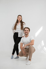 Studio photo session. The girl stands and rests her hand on the shoulder of the guy who is squatting. A good couple. Friends, colleagues, brother and sister. Smiling people