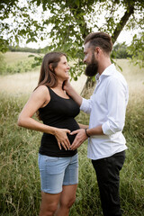 pretty young pregnant woman with black shirt is standing with her boyfriend in a high meadow and they are happy and full of anticipation for the baby