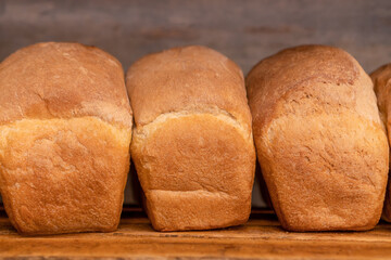 Close-up of freshly baked bread on wooden shelves, front view. Production of bakery products