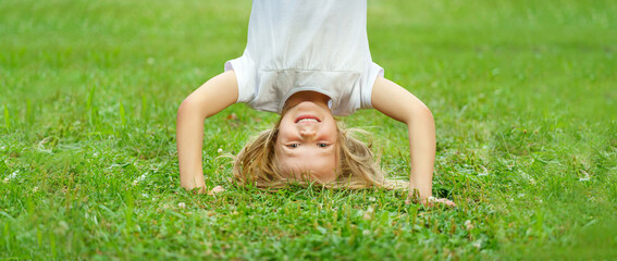 A sweet little girl in summer stands upside down. Happy carefree childhood in nature.