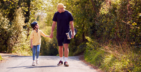 Father And Daughter With Skateboard Walking Along Country Road Together