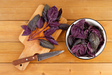 Purple basil leaves on the cutting board and in a bowl on a wooden kitchen table. Top view.