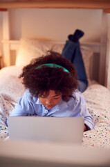 Boy In Bedroom At Night Lying On Bed Using With Laptop With Illuminated Globe