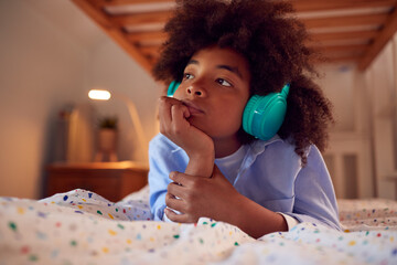 Boy Thinking In Bedroom Lying On Bed Wearing Headphones