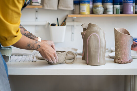 Ceramics workshop. Cropped photo of woman artisan making earthenware mug, working with clay during pottery masterclass, tattooed hands of female ceramist sculpting or modeling handicrafter kitchenware