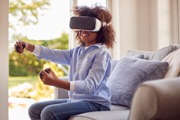 Boy Sitting On Sofa In Lounge Wearing VR Headset Playing Game