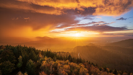 The sun shines through a gap in the cloudy sky and colours a departing thunderstorm in golden shades