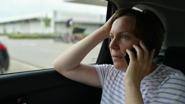 Casual serious woman talking on mobile phone while sitting in parked car on parking lot