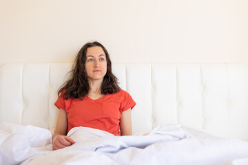 Obraz na płótnie Canvas A girl in red pajamas sits on a white bed
