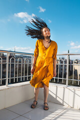 a smiling woman stands on a roof overlooking the city and the wind inflates her dress