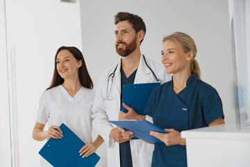 Portrait of a group of happy doctors and nurses standing near reception in hospital and looking away