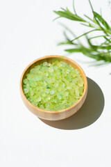 Wooden bowl with green bath sea salt with rosemary branch shadows. Beauty treatment for spa and wellness on white background. Skincare natural cosmetic concept for body care