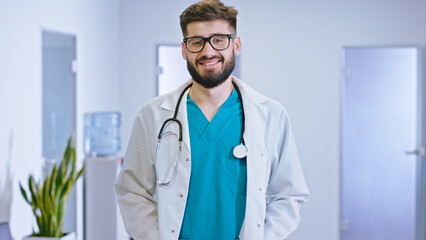 Portrait of a young man doctor in the hospital corridor looking straight to the camera smiling large