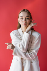 young woman in white blazer looking at camera isolated on crimson.
