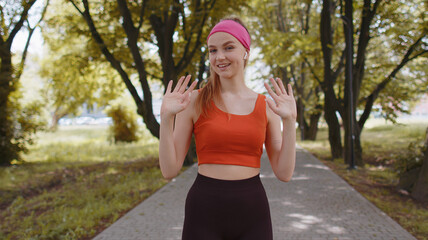 Wow. Hello, welcome. Athletic fit slim runner girl waving hi with her palm greeting with hospitable friendly smile. Young woman workout cardio training in park at morning. Active healthy sportswoman