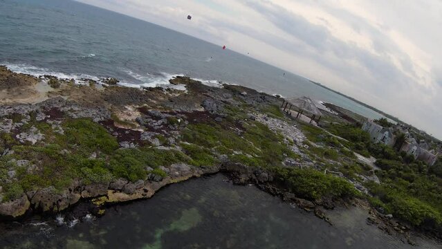 Drone footage of coastal rocks separating the Caribbean ocean and a small lagoon in Quintana Roo, Mexico with people parasailing in background.