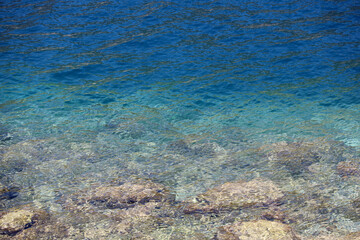 Transparent sea surface with stones on a bottom. Rocky beach, turquoise water for background