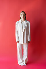 full length of woman in white suit and socks on crimson background.