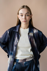 trendy young woman holding hands behind back and looking at camera isolated on beige.