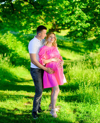 Fototapeta premium Beautiful young couple of a man and a pregnant woman in the forest at sunset