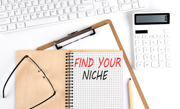 Notebook with the word FIND YOUR NICHE with keyboard and calculator on the white background