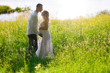 Beautiful young pregnant woman with her husband in the forest at sunset on a picnic sitting on the grass