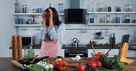woman wiping irritated eyes near chopped onion on chopping board.