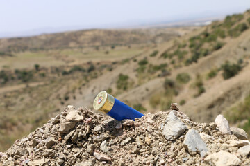 Used blue shotgun cartridge on mountain background