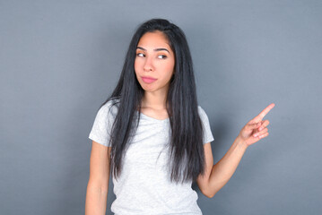 young beautiful brunette woman wearing white t-shirt over grey background points at copy space and advertises something, advices best price.