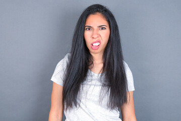 Portrait of dissatisfied young beautiful brunette woman wearing white t-shirt over grey background...