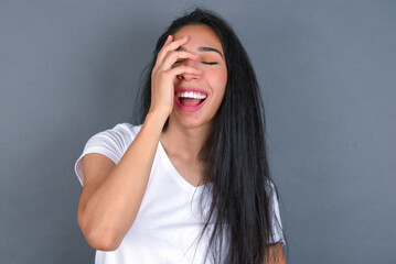 Charismatic carefree joyful young beautiful brunette woman wearing white t-shirt over grey background likes laugh out loud not hiding emotions giggling hear funny hilarious joke chuckling facepalm.