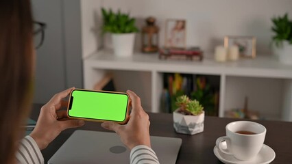 Green screen chromakey smartphone phone display. Young woman is holding phone in her hands at desk at home. Freelancer, student working remotely. Video calling chat connection. Chromakey Mock-Up