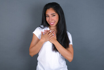 Honest young beautiful brunette woman wearing white t-shirt over grey background keeps hands on...