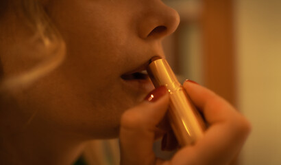 horizontal closeup with selective focus on woman putting her lipstick on her lips with very carefully, copy space.