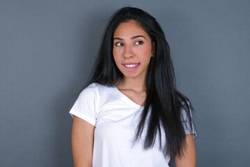 young beautiful brunette woman wearing white t-shirt over grey background with thoughtful...