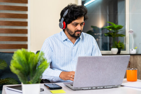 Young man with wireless headphones working on laptop while sitting at office - concept of online meeting, working lifestyles and employment