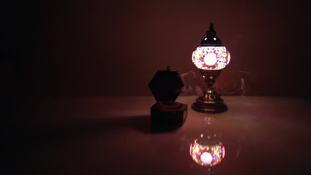 Arabian lamp next to a vessel containing incense lit with smoke on a table with dim warm light