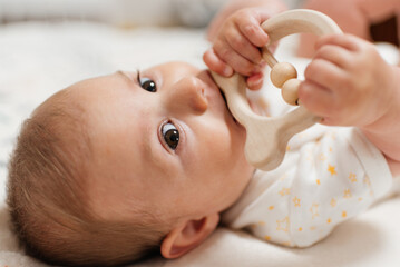 The child is gnawing on a wooden toy, a teether