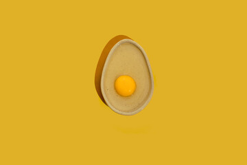 Avocado shaped ceramic plate with raw egg yolk on a bright yellow color background with copy space. Healthy dieting idea.