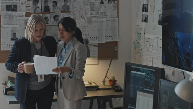 Medium long tracking left slowmo of mature blonde Caucasian woman and young Hispanic female colleague standing in office at daytime, special agents talking