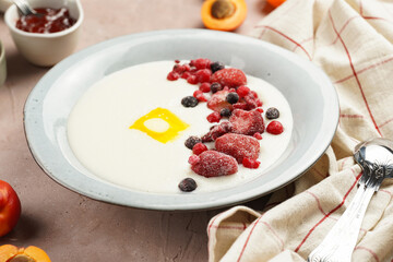 Traditional breakfast semolina porridge - creamy pudding with butter, frozen berries and fresh apricots in a grey plate