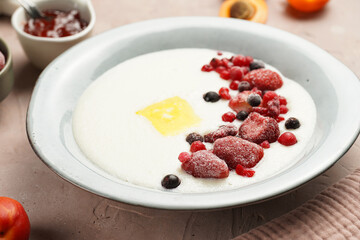Traditional breakfast semolina porridge - creamy pudding with butter, frozen berries and fresh apricots in a grey plate