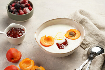 Traditional breakfast semolina porridge - creamy pudding with butter, jelly, frozen blueberries and fresh apricots in an oval plate on linen kitchen towel