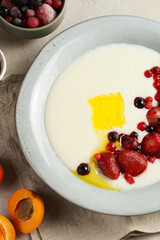 Traditional breakfast semolina porridge - creamy pudding with butter, frozen berries and fresh apricots in a grey plate