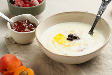 Traditional breakfast semolina porridge - creamy pudding with butter, frozen blueberries and fresh apricots in an oval plate on checkered kitchen towel