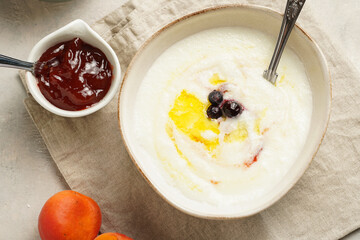 Traditional breakfast semolina porridge - creamy pudding with butter, frozen blueberries and fresh apricots in an oval plate on checkered kitchen towel
