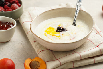 Traditional breakfast semolina porridge - creamy pudding with butter, frozen blueberries and fresh apricots in an oval plate on checkered kitchen towel
