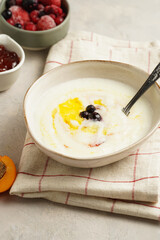 Traditional breakfast semolina porridge - creamy pudding with butter, frozen blueberries and fresh apricots in an oval plate on checkered kitchen towel