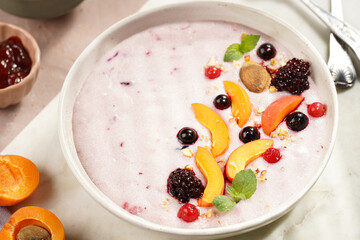 Traditional breakfast semolina porridge - purple creamy pudding with apricot slices, frozen berries, fresh mint, jelly on marble board